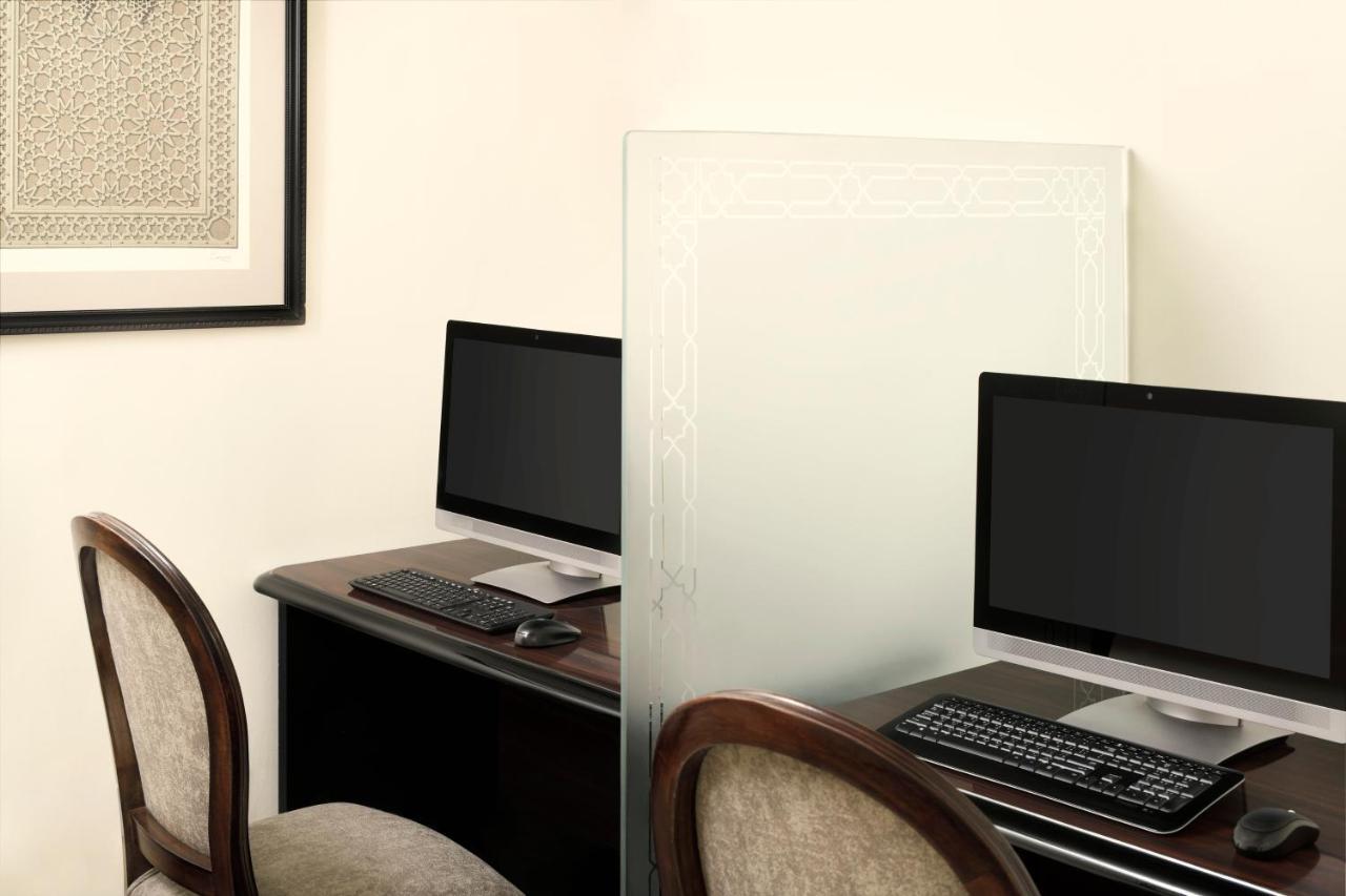 Hotel Intercontinental Dar Al Iman Madinah By Ihg Medína Exteriér fotografie The photo shows a workspace featuring two computers set up on a dark wooden desk. Each computer has a monitor and a keyboard. A frosted glass partition is placed between the two workstations, providing some privacy. In the background, there is a fram