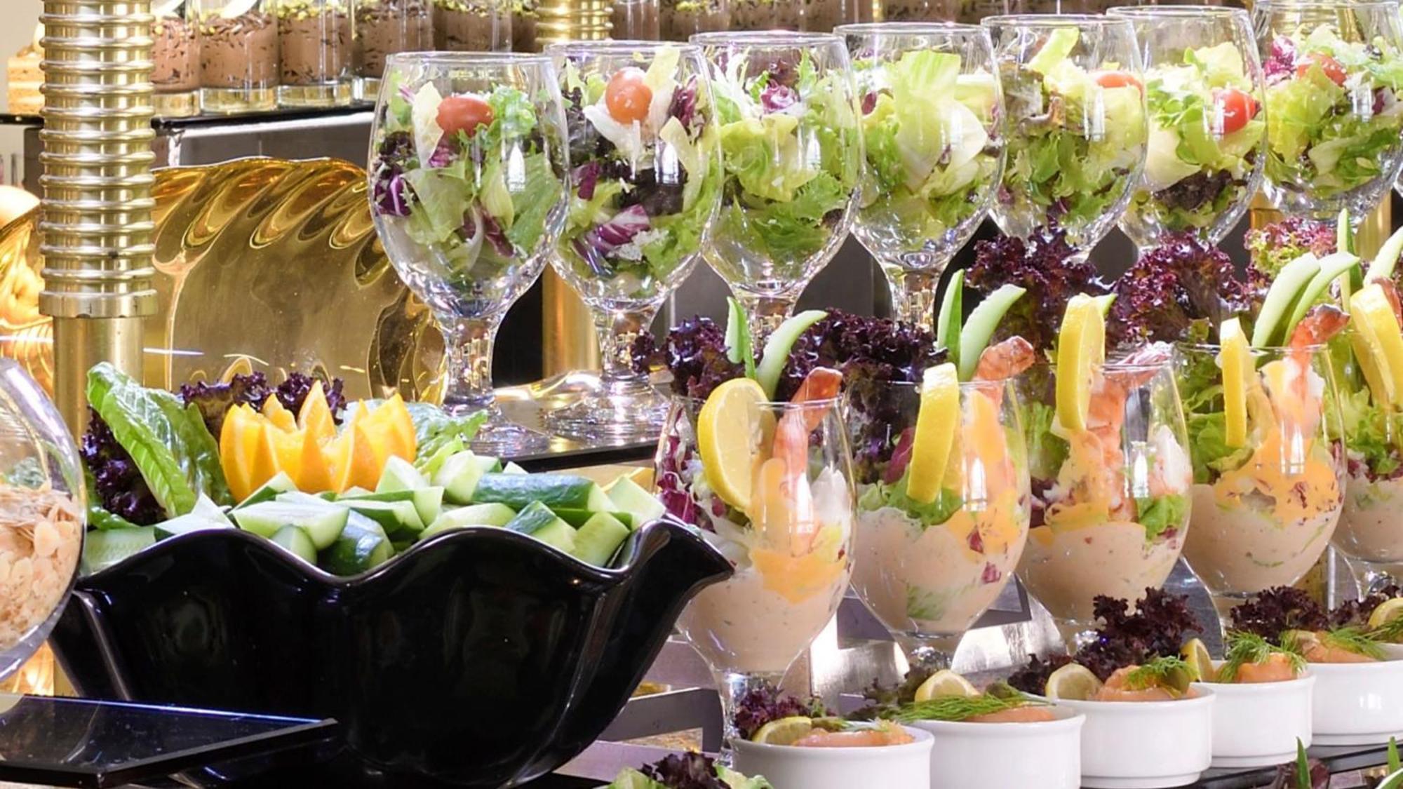 Hotel Intercontinental Dar Al Iman Madinah By Ihg Medína Exteriér fotografie The photo features an elegant display of food items. In the background, there are several clear glasses filled with vibrant salads, featuring various types of greens and garnishes. In the foreground, there is a decorative black bowl containing cut pi