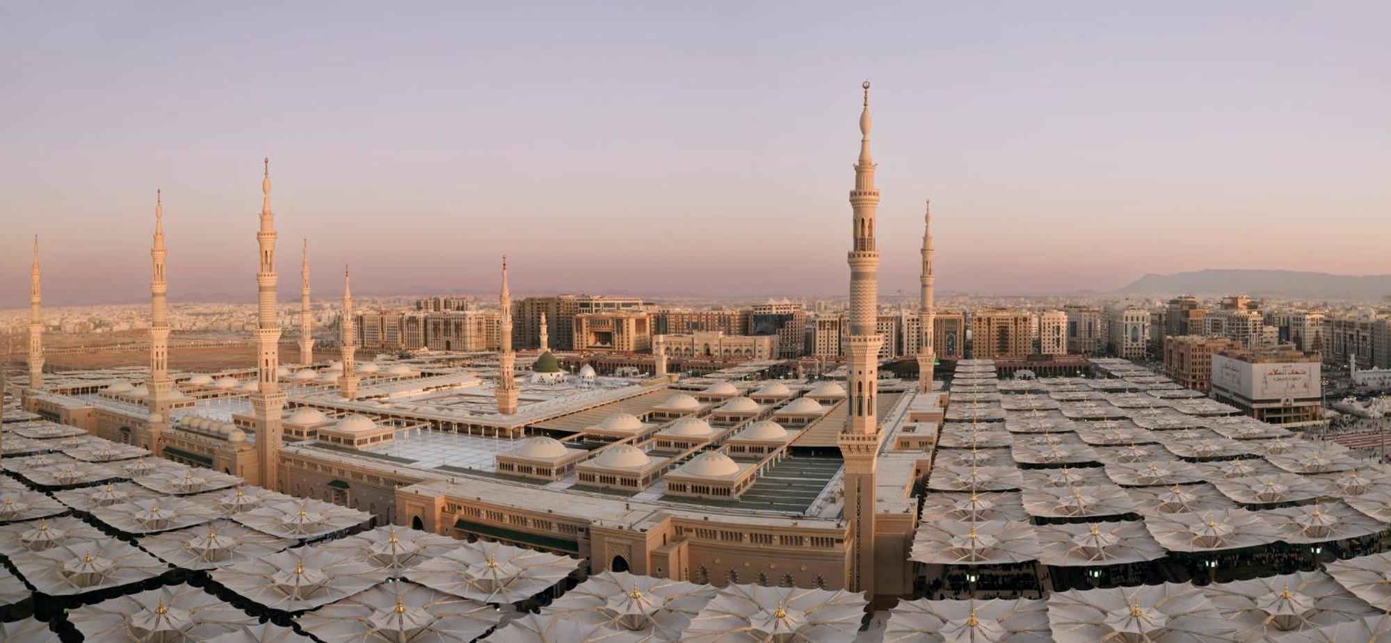Hotel Intercontinental Dar Al Iman Madinah By Ihg Medína Exteriér fotografie The photo shows an aerial view of the Al-Masjid an-Nabawi, or the Prophet's Mosque, located in Medina, Saudi Arabia. The mosque features distinct minarets, large white domes, and expansive open areas with large umbrellas that provide shade for visito