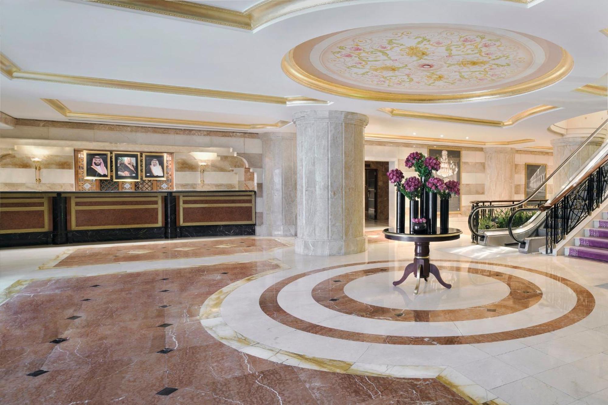 Hotel Intercontinental Dar Al Iman Madinah By Ihg Medína Exteriér fotografie The photo shows a luxurious hotel lobby. The space features elegant marble flooring with circular designs, complemented by a large, decorative ceiling. In the center, there is a round table adorned with a floral arrangement. Behind the table, a recep