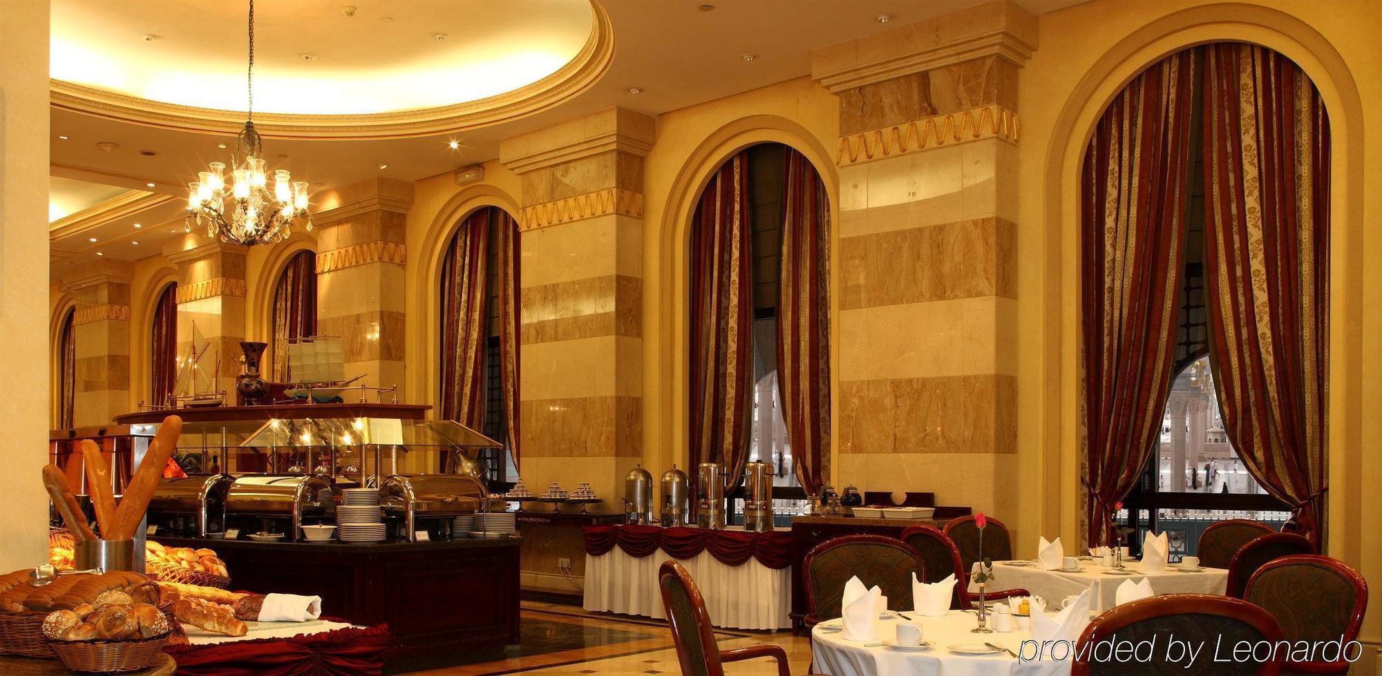 Hotel Intercontinental Dar Al Iman Madinah By Ihg Medína Restaurace fotografie The photo shows an elegant dining restaurant interior. It features stylish arches and walls with a blend of marble and decorative elements. There are large windows draped with rich curtains, contributing to the luxurious atmosphere. The dining area i