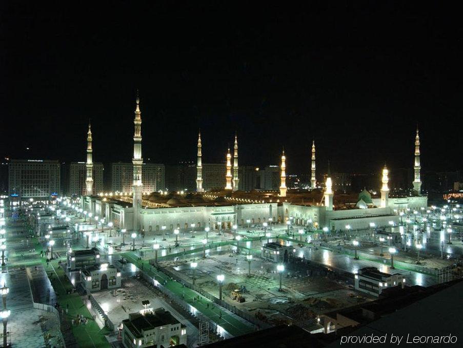 Hotel Intercontinental Dar Al Iman Madinah By Ihg Medína Vybavení fotografie The image shows the illuminated landscape of a mosque complex at night. It features several tall minarets, which are typically part of Islamic architecture, adorned with lights. The mosque's central building is also brightly lit, surrounded by an ope